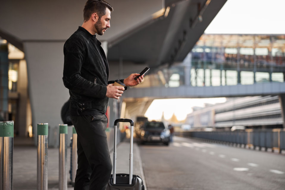 Reisender mit Smartphone und Kaffee – Park & Fly für Geschäftsreisen in Wien